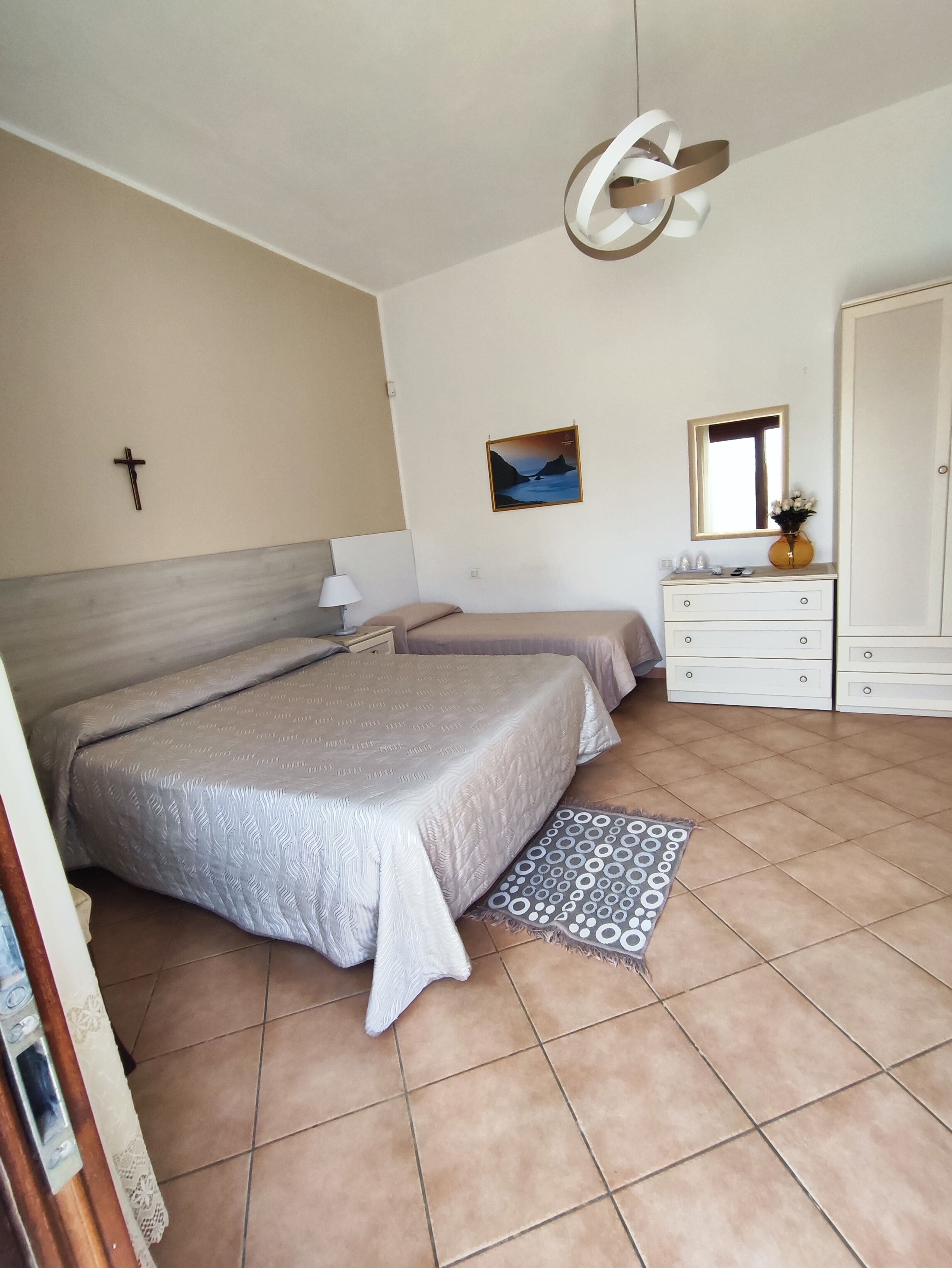 Un dormitorio con dos camas, una mesita de noche, un aparador, un espejo y una cruz colgada en la pared.
