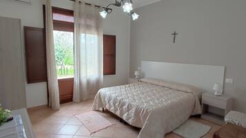 A bedroom with a bed, bedside tables, a lamp, a cross on the wall, and a window with curtains.
