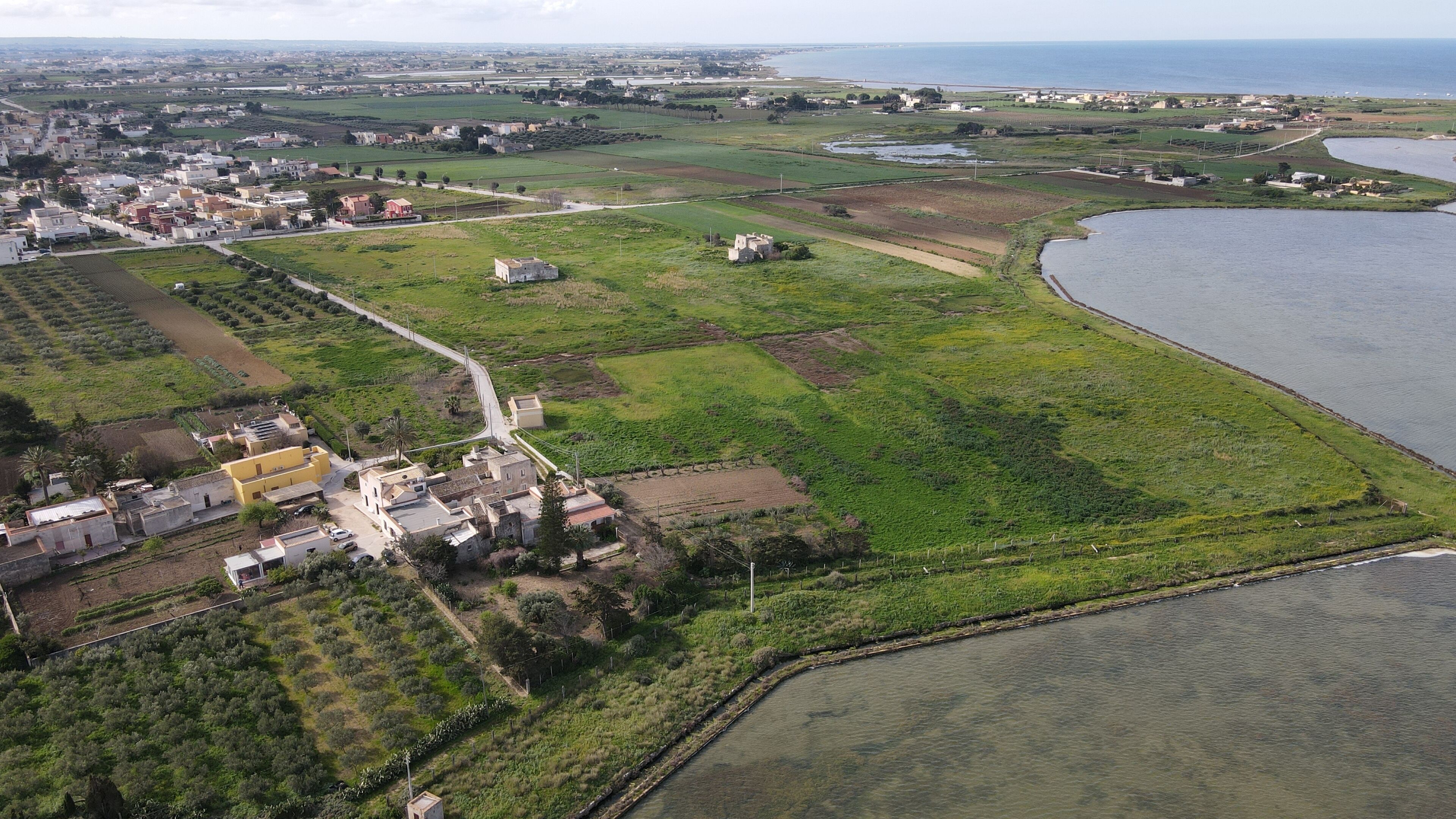 An aerial view of a coastal town with a mix of residential and agricultural areas, a main road, and a large body of water.