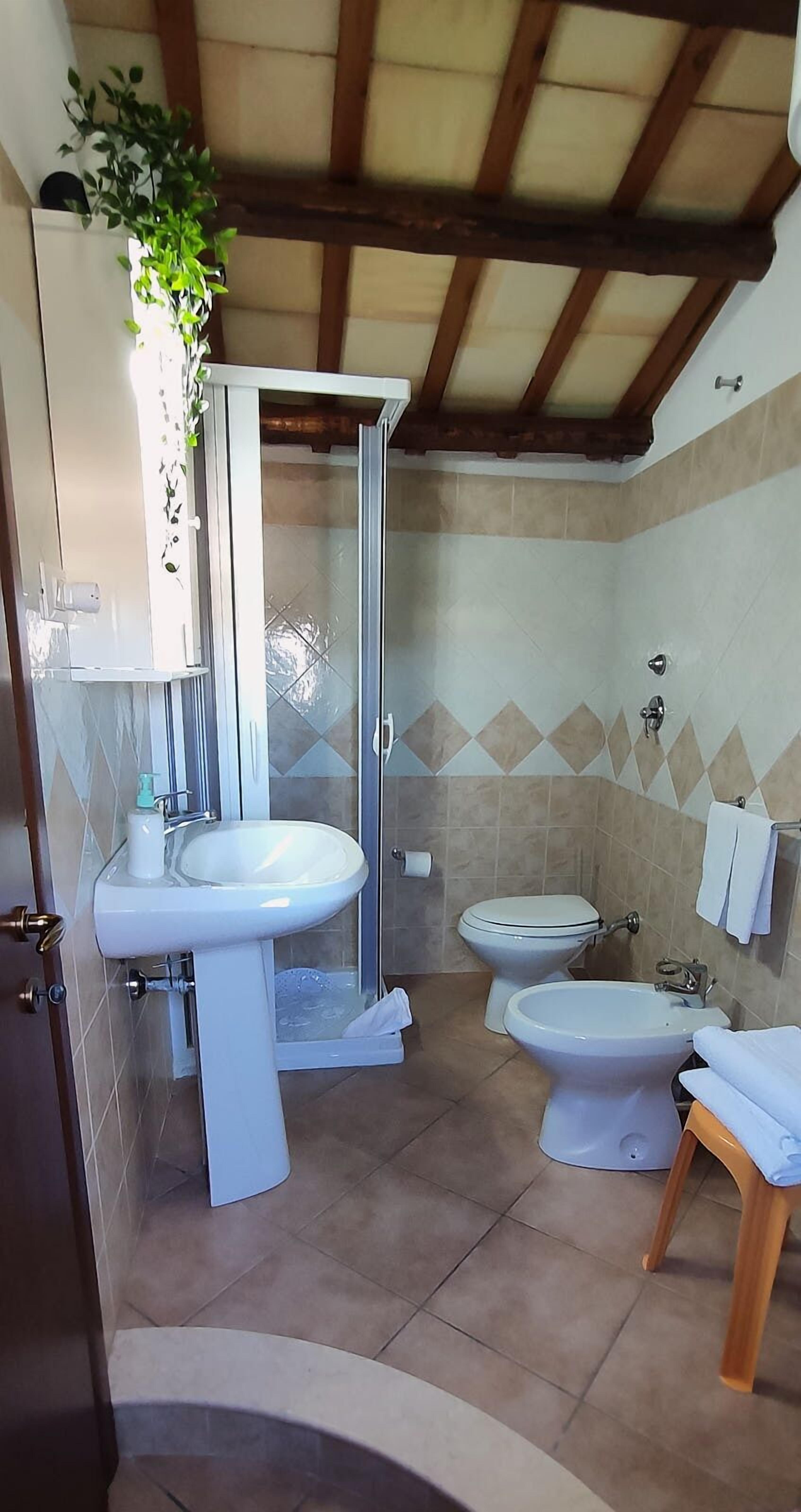 A bathroom with a sink, two toilets, a bidet, a shower, and a wooden stool.