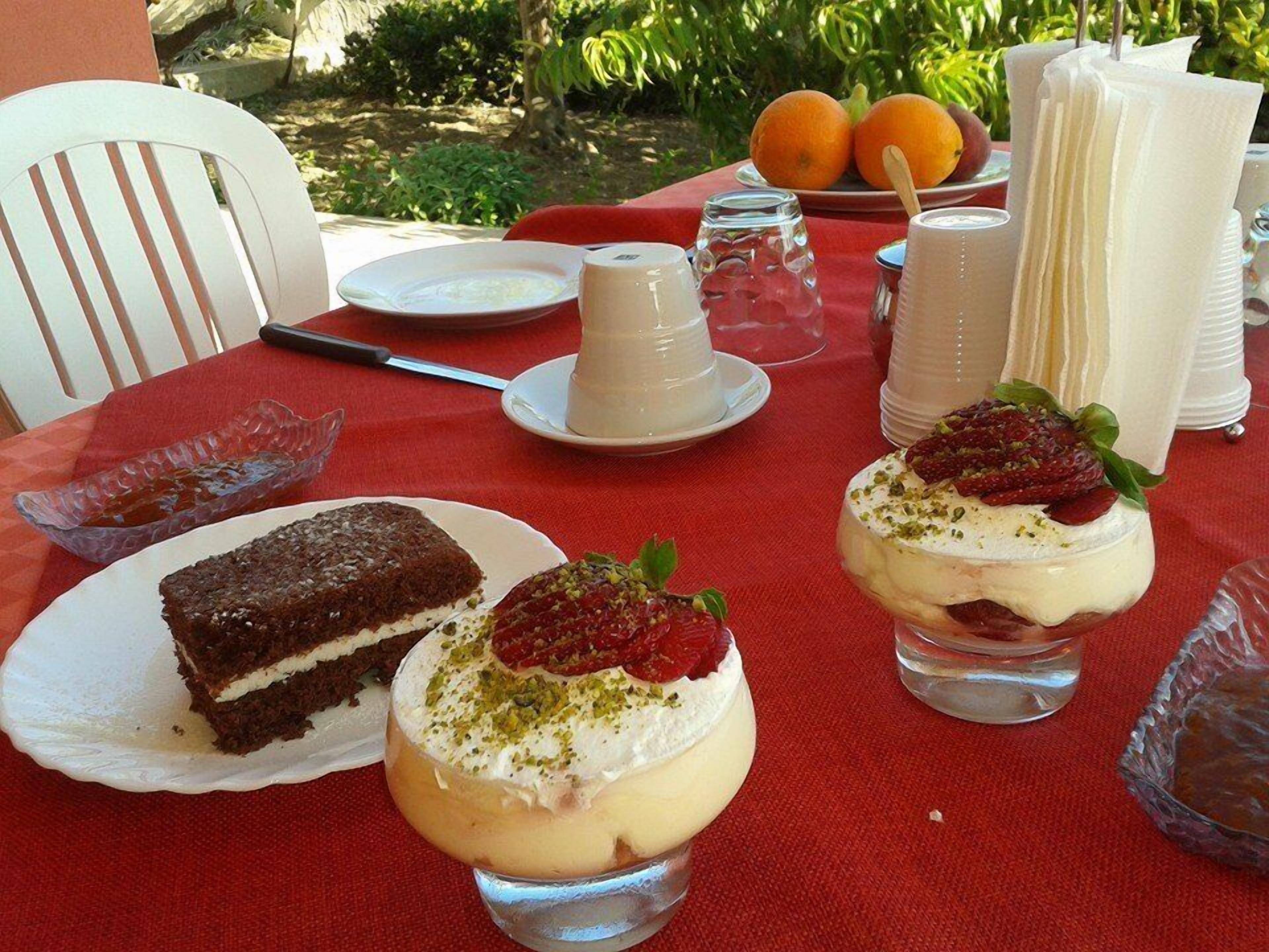 A table set outdoors with desserts, a plate of oranges, and a red tablecloth.