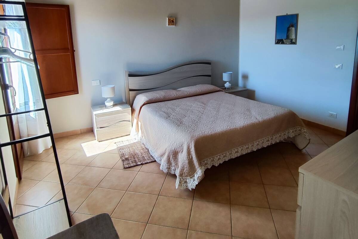 Ein Schlafzimmer mit Bett, Nachttisch, Stuhl, Holzboden und einem Fenster.