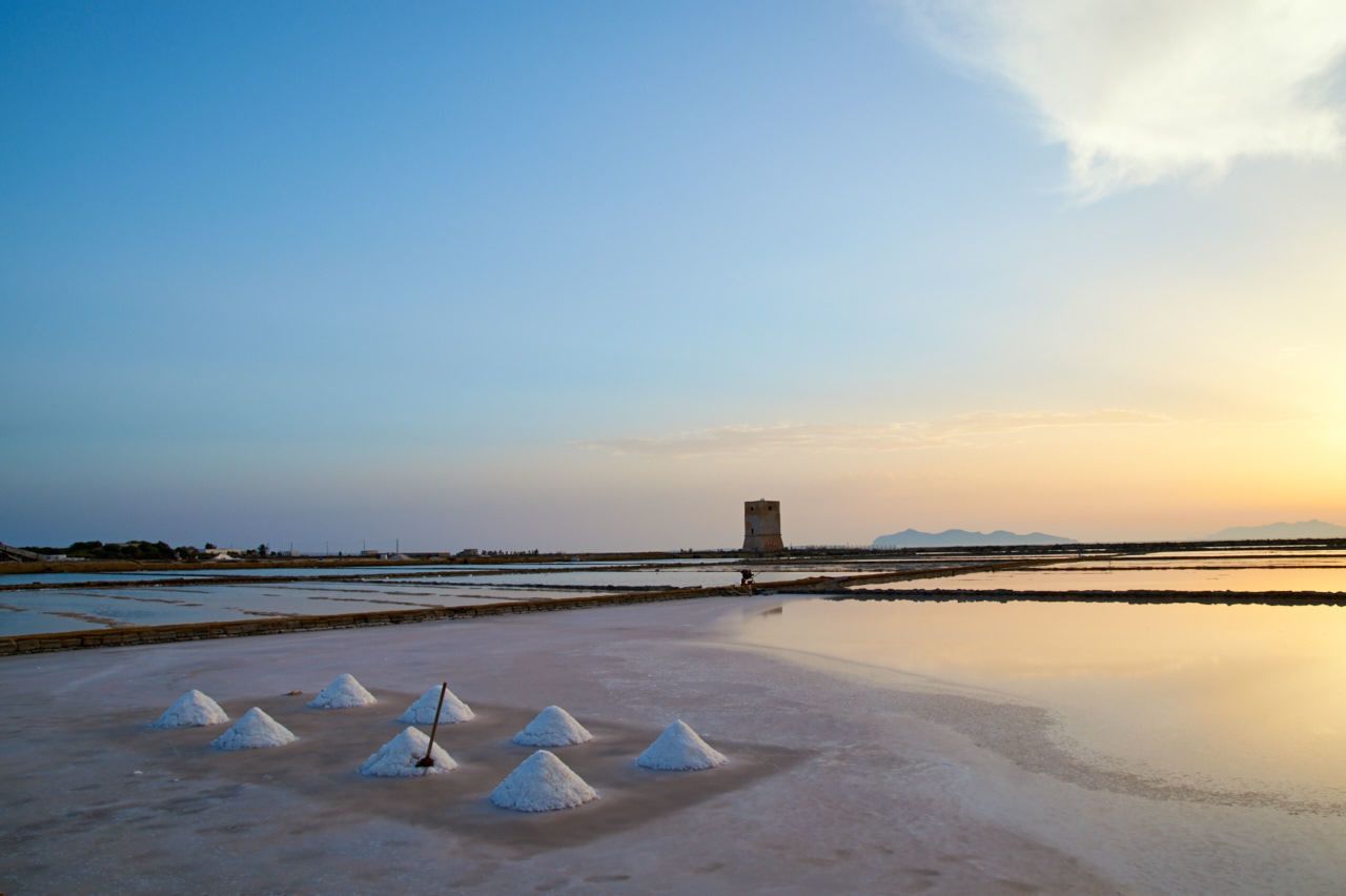 Una salina con formaciones de sal blanca y una torre al fondo.