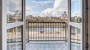 Vista desde un balcón con baranda de metal que da a un río y edificios de arquitectura con cúpulas.