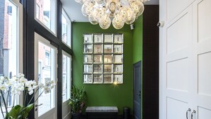 Un pasillo con una pared verde, un banco, una araña y un espejo grande.