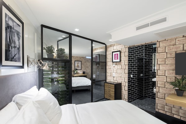 A modern hotel room with a bed, a desk, and a large mirror. There is a brick-patterned wall and a black brick wall with text.