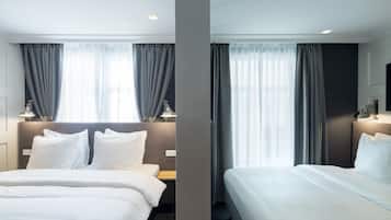 A hotel room with two beds, a nightstand, a lamp, and a window with curtains.