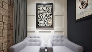 Una habitación con dos sillones grises frente a una mesa, una carta de vinos enmarcada en la pared y un papel tapiz con diseño.