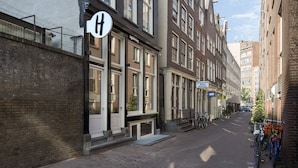 Una calle estrecha bordeada de edificios tradicionales europeos, con un letrero prominente en forma de 'H', que indica un hotel.