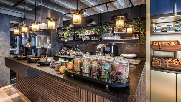 Un área de bar moderna con una encimera negra, frascos de vidrio con aperitivos y lámparas colgantes.