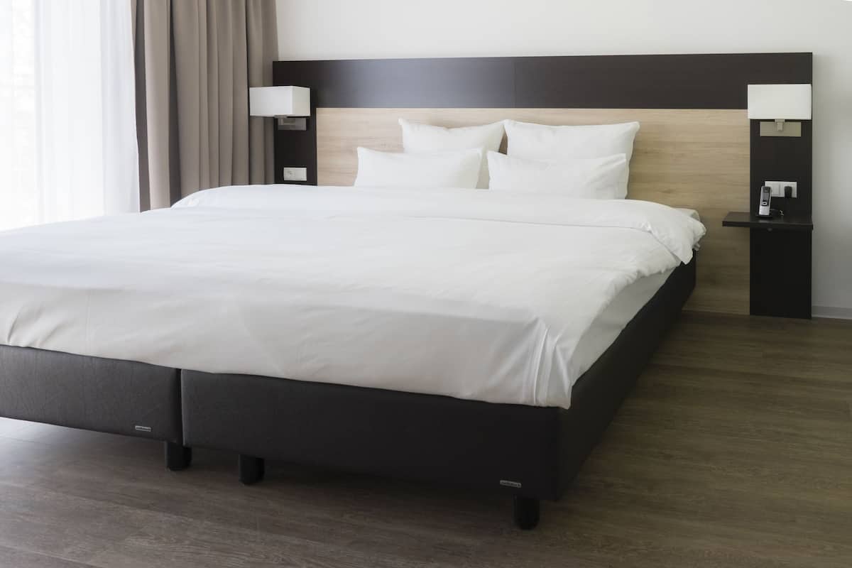 A modern hotel room with a large bed, dark headboard, and two bedside tables with lamps.
