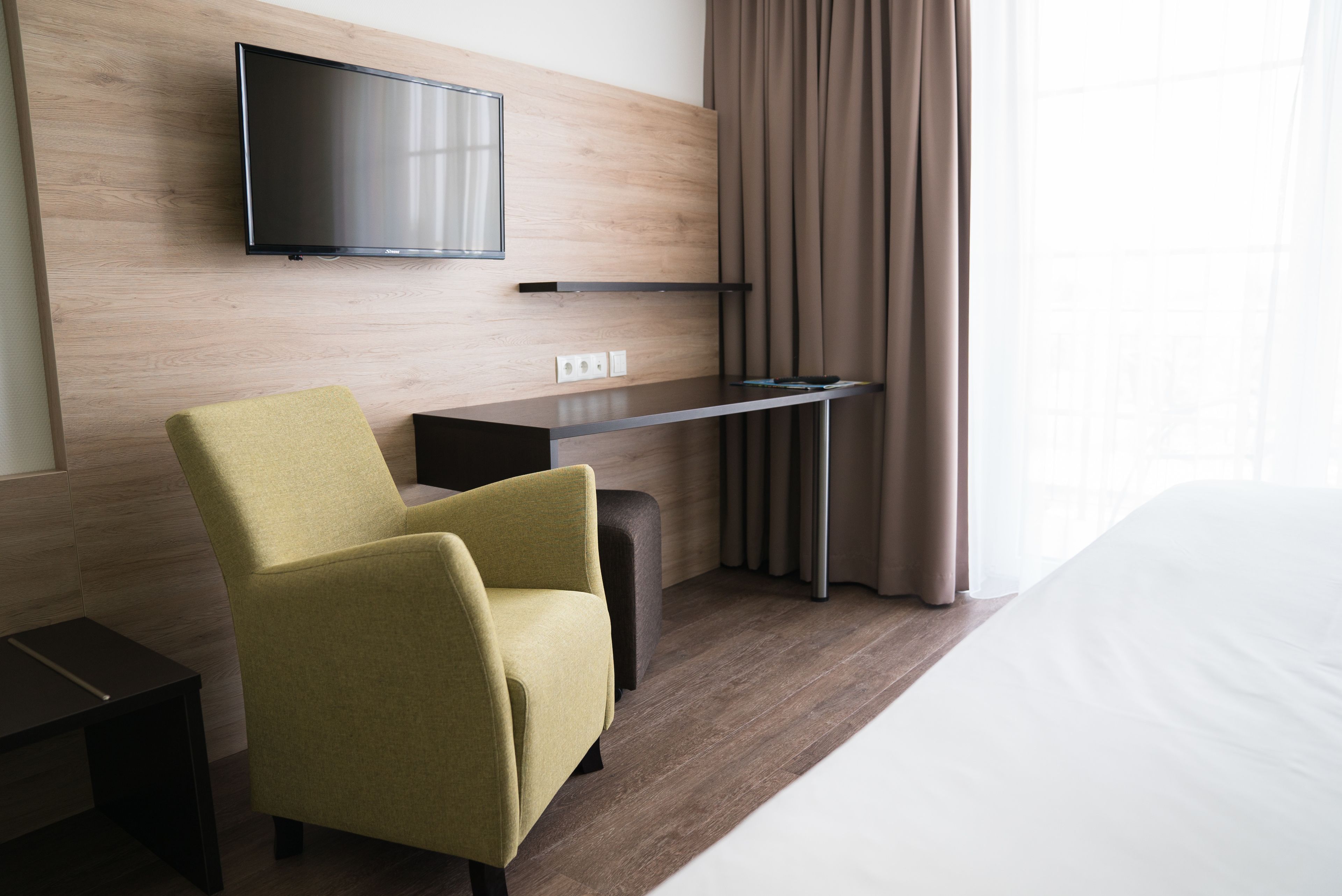 Una habitación de hotel moderna con una televisión de pantalla plana montada en la pared, un escritorio con una silla y una cama.