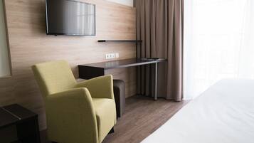Una habitación de hotel moderna con una televisión de pantalla plana montada en la pared, un escritorio con una silla y una cama.