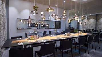 Un espace de restauration moderne, doté de plusieurs tables et chaises, de luminaires suspendus et d’un grand miroir mural.