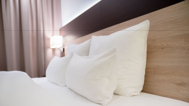Un lit bien fait, avec une literie et des oreillers blancs, une tête de lit en bois et un luminaire fixé au mur.