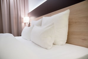 A neatly made bed with white bedding and pillows, a wooden headboard, and a wall-mounted light fixture. - Taste Style Bären Auggen (Auggen)