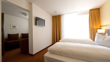 A hotel room with two beds, a television, a desk, and a window with curtains.
