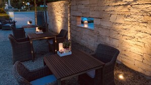 Une terrasse extérieure agrémentée de meubles en osier et de murs en pierre, avec des tables décorées de bougies et de plantes en pot.