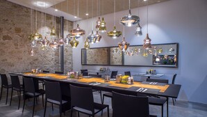 Un espace de salle à manger moderne, avec une longue table, des chaises noires et plusieurs lampes suspendues.