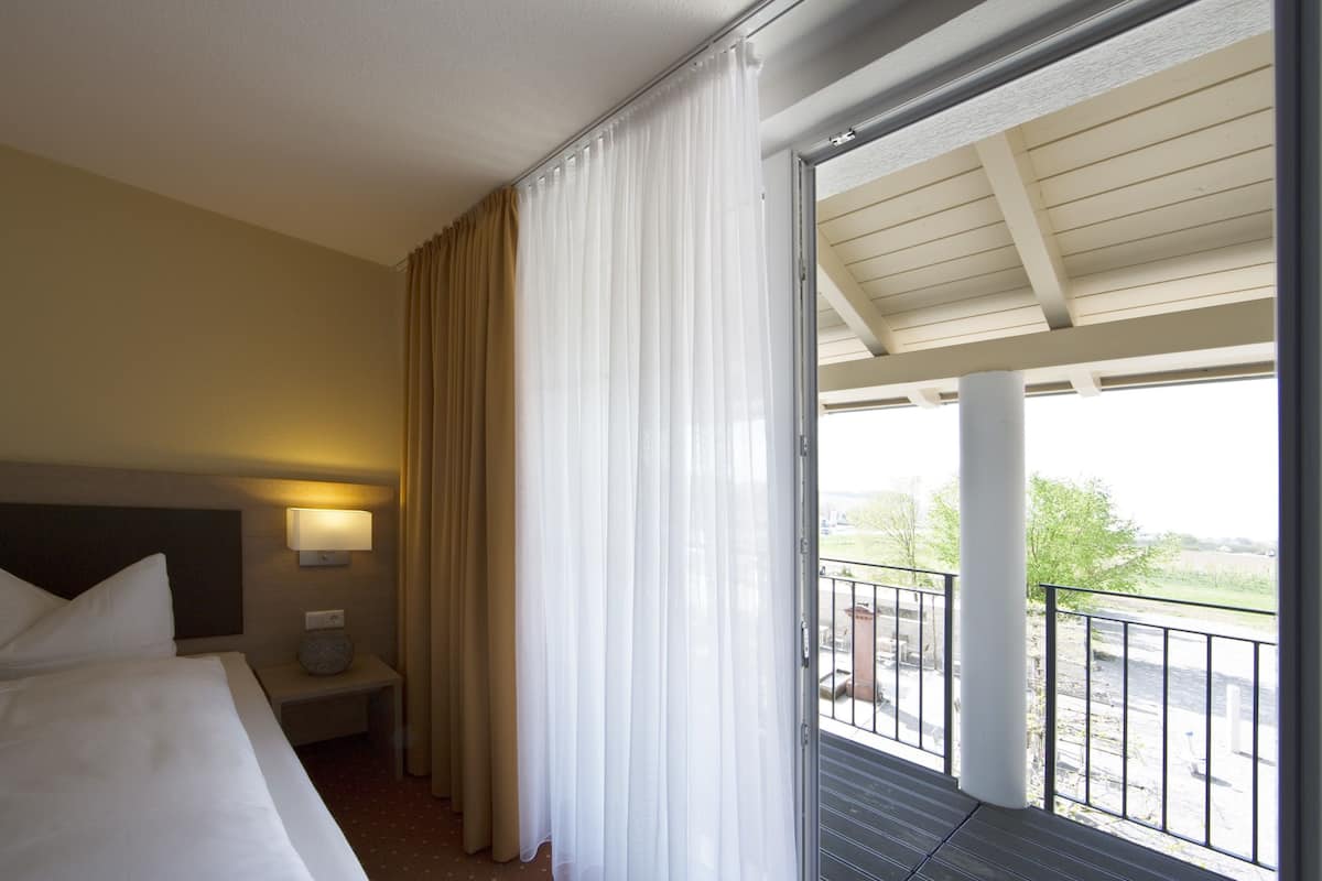 A hotel room with a bed, a nightstand, a lamp, a window with curtains, and a balcony.