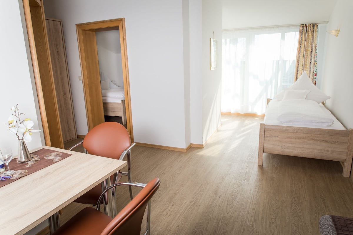 Habitación de hotel con una cama de madera, un escritorio con una silla, una pequeña mesa con un jarrón de flores y un espejo.