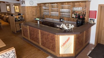 Uma área de bar com balcão de madeira, copos e garrafas.