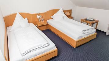 A hotel room with two single beds, a small bedside table with a lamp, a clock, and a wall-mounted shelf with a vase and decorative items.