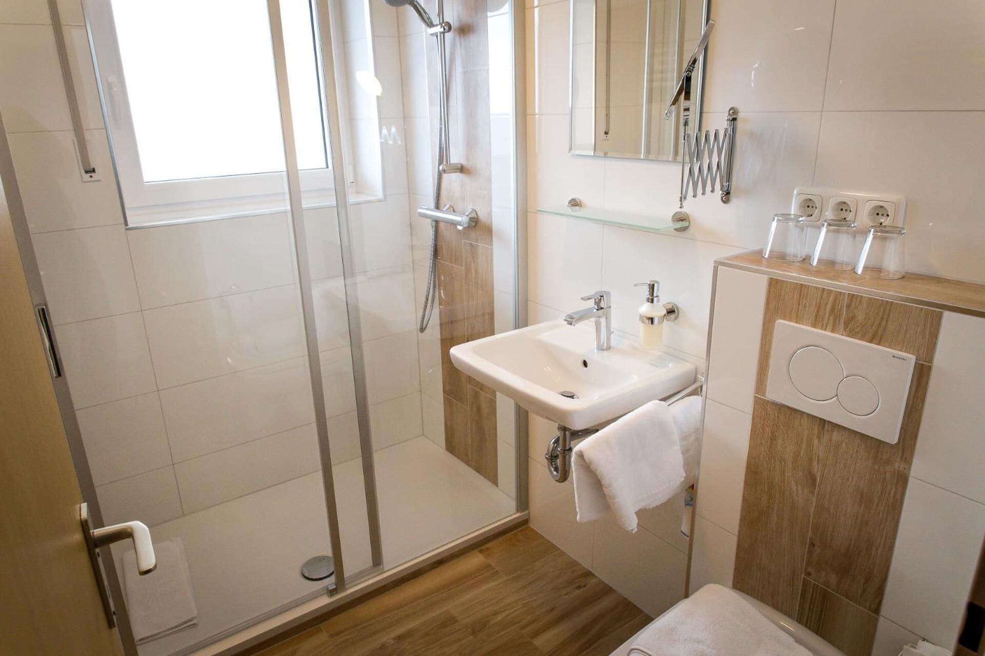 Un baño moderno con cabina de ducha de vidrio, un lavabo con espejo y un mueble de tocador de madera con una toalla colgada en la pared.
