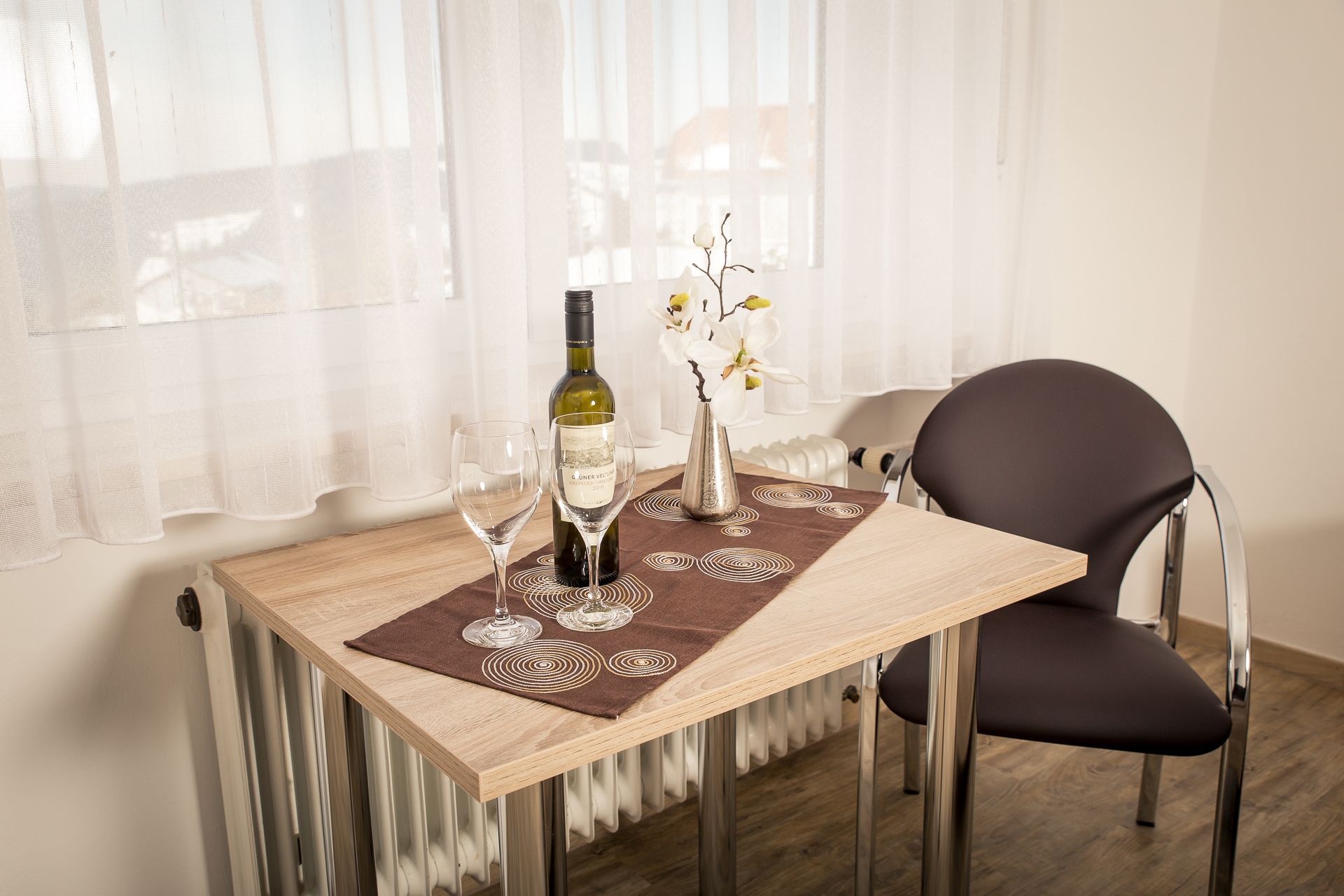 A dining table with a bottle of wine, two wine glasses, and a vase with flowers.