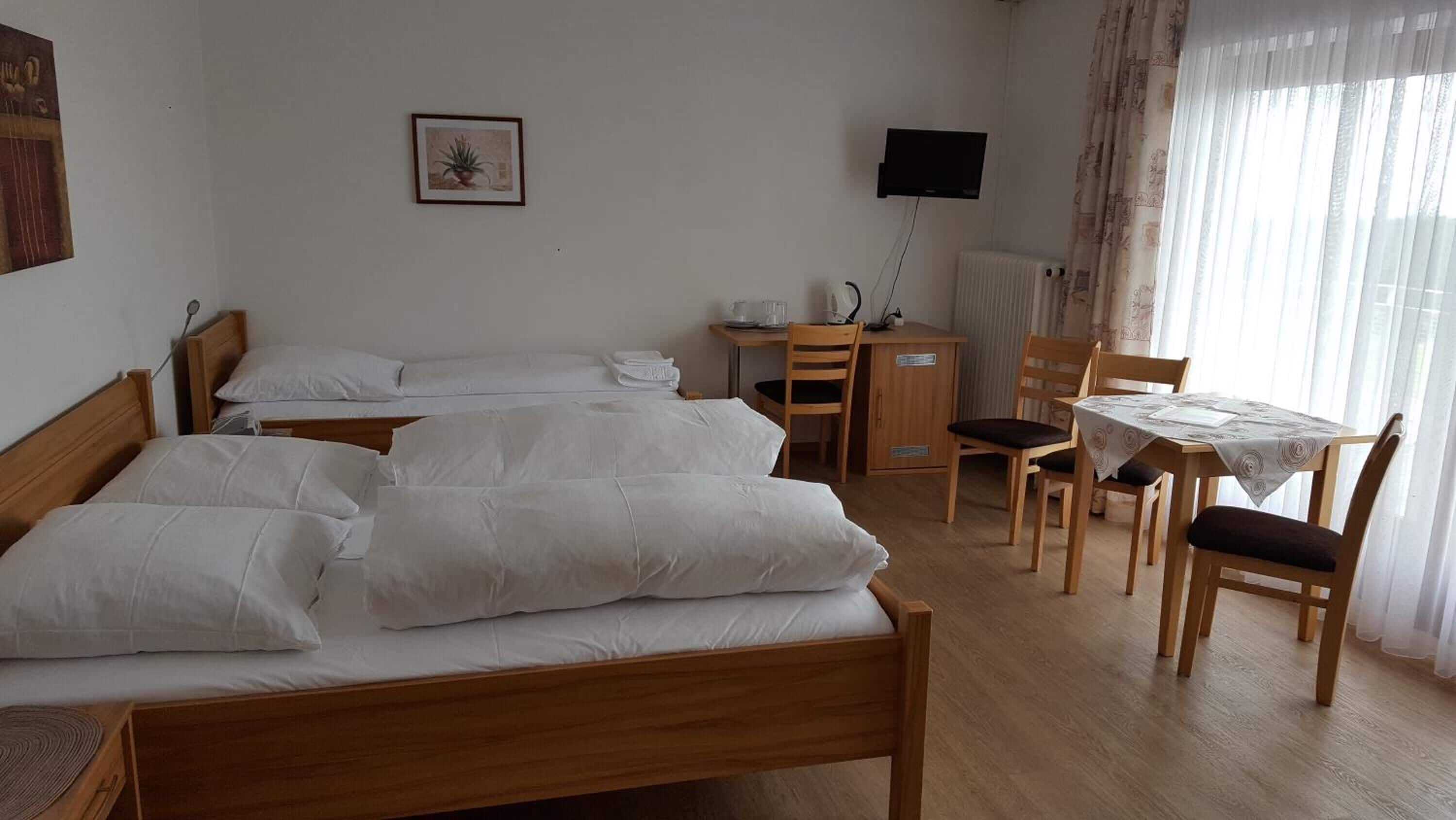 Hotellihuone, jossa on kaksi puista sänkyä, työpöytä tuolilla, televisio ja ikkuna, jossa on verhot.