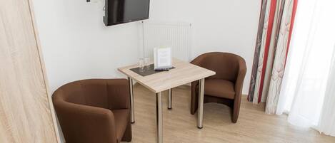 A small room with a wooden table, two brown chairs, a flat-screen TV mounted on the wall, and a radiator.