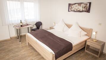 Quarto arrumado com cama de madeira, mesa de cabeceira, cadeira, escrivaninha e radiador.
