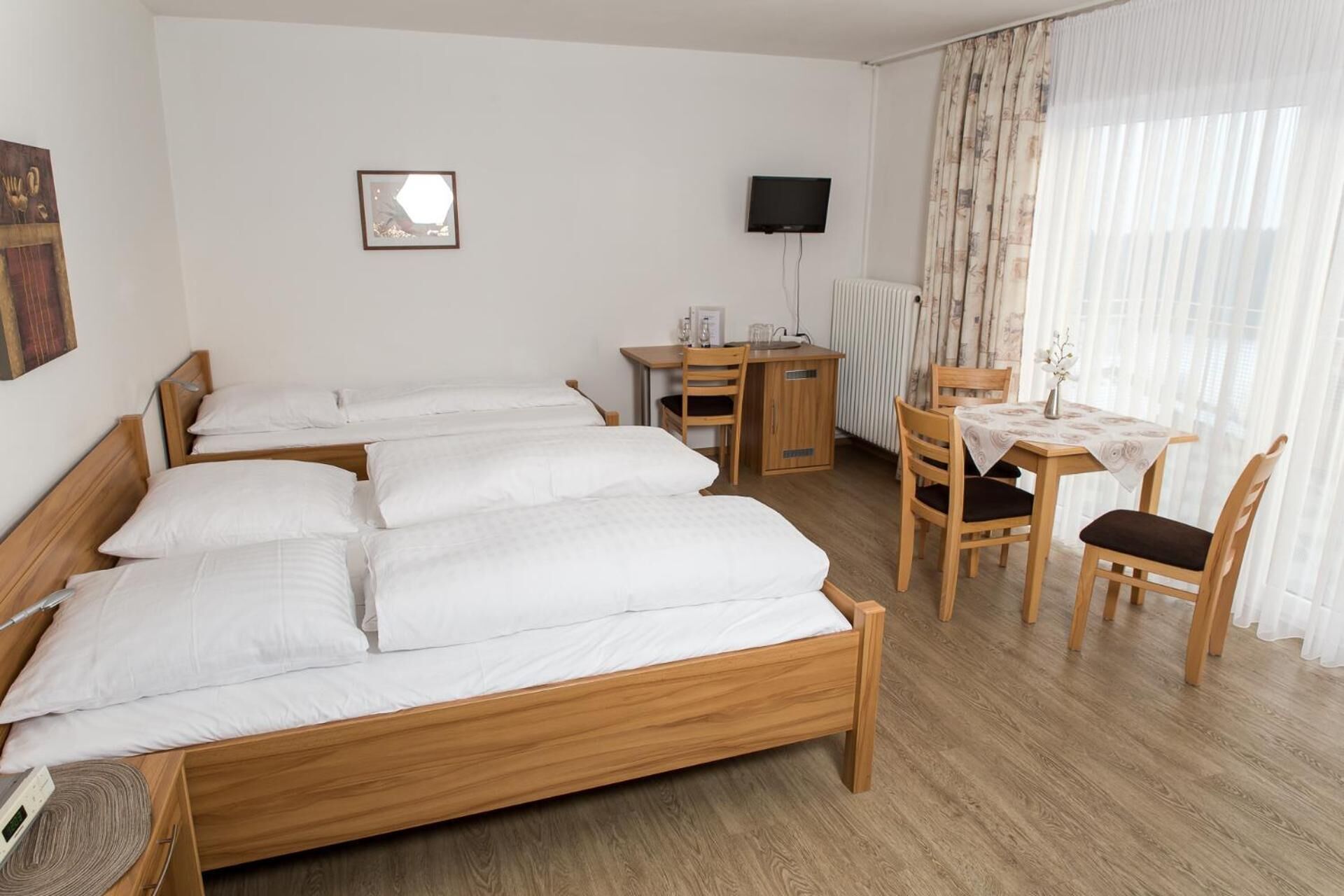 Habitación de hotel con dos camas de madera, un escritorio con silla, televisor y ventana con cortinas traslúcidas.