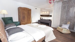 Une chambre à coucher moderne avec un grand lit, une armoire en bois, un fauteuil vert et une chaise en osier.