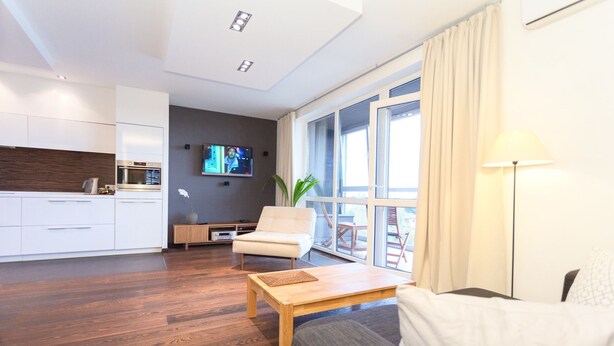 Un salon moderne avec un canapé, une table basse et un téléviseur. Il y a également un coin cuisine avec des meubles blancs et un plancher en bois.