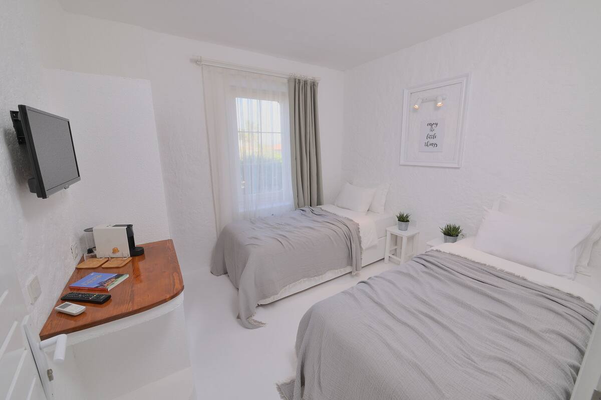 A bedroom with two beds, a desk with a computer, a TV, and a window with curtains.