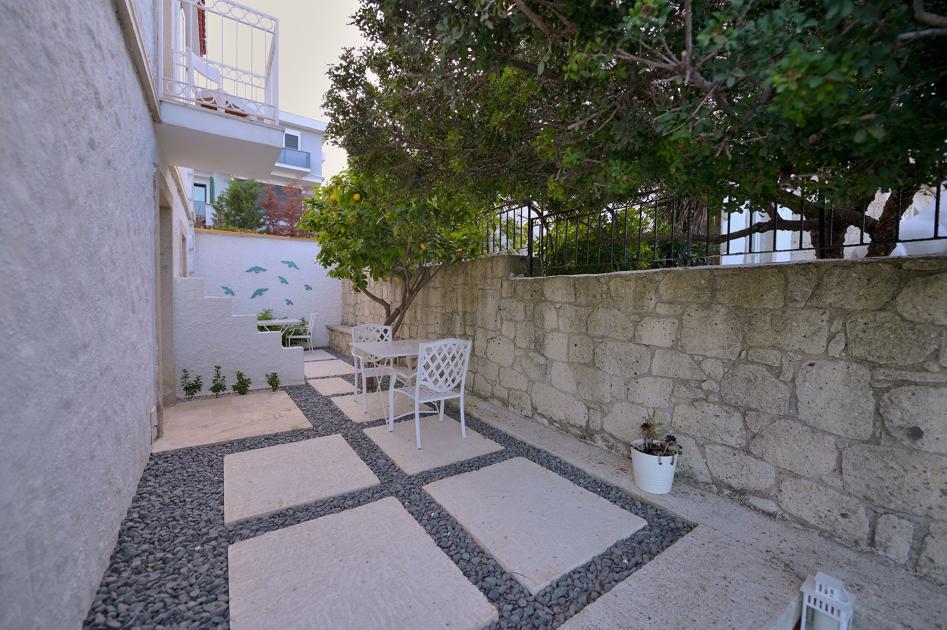A courtyard with a stone wall, a white fence, and a potted plant.