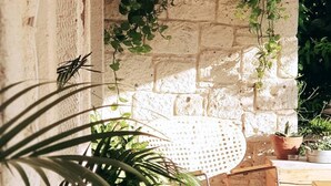 Un espacio al aire libre rústico con cestas de mimbre colgando del techo, una silla tejida y plantas en macetas.