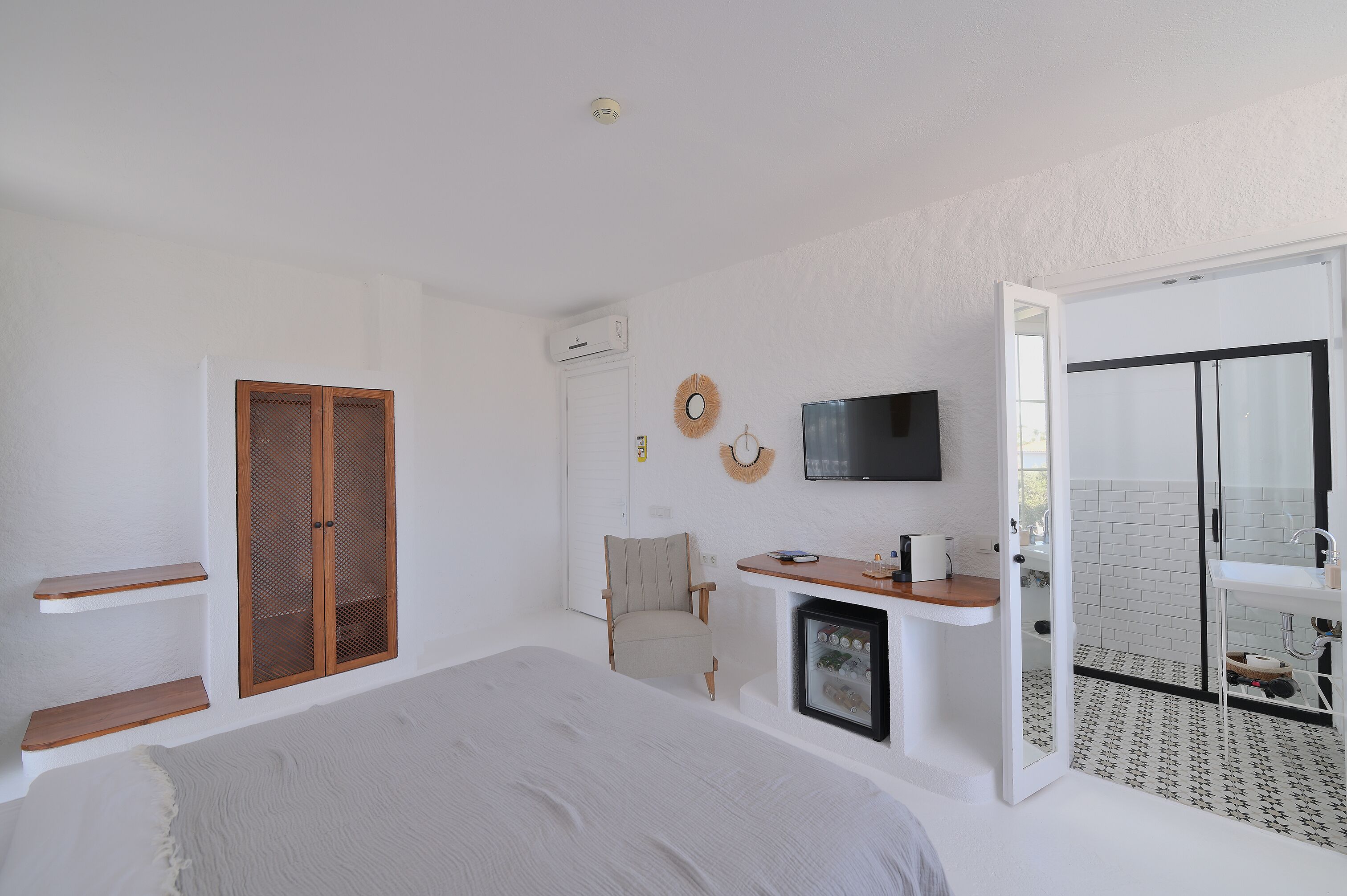 A bedroom with a bed, a TV, a chair, a small table, and a bathroom with a shower and toilet.