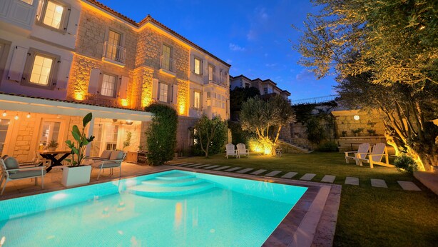 Zona de piscina con pileta, mobiliario exterior y un edificio de piedra con varias ventanas y balcones.