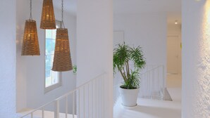 Un pasillo interior blanco con tres lámparas colgantes de mimbre, una planta en maceta y una barandilla blanca.