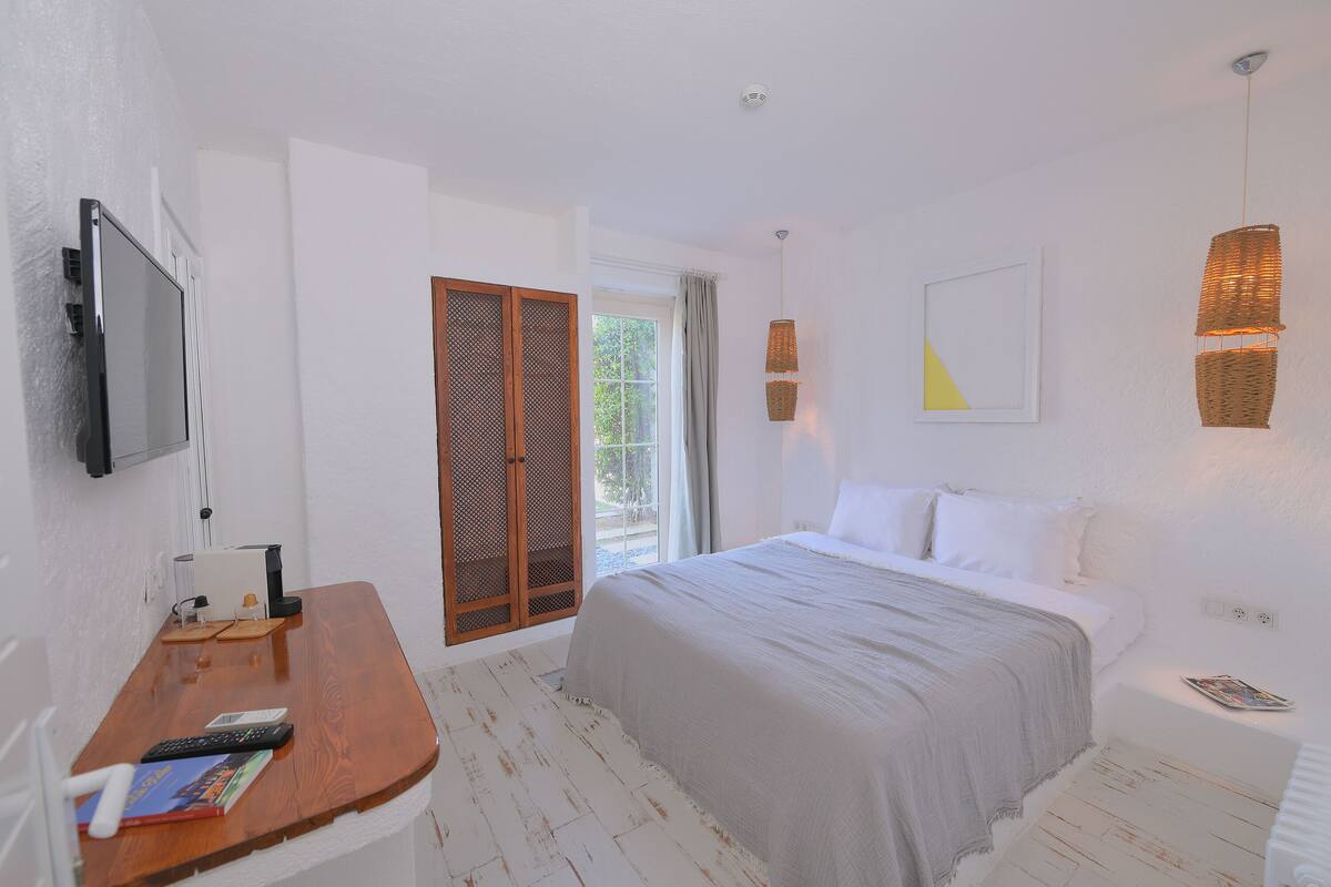 A bedroom with a bed, a desk with a TV, a window, and a door.