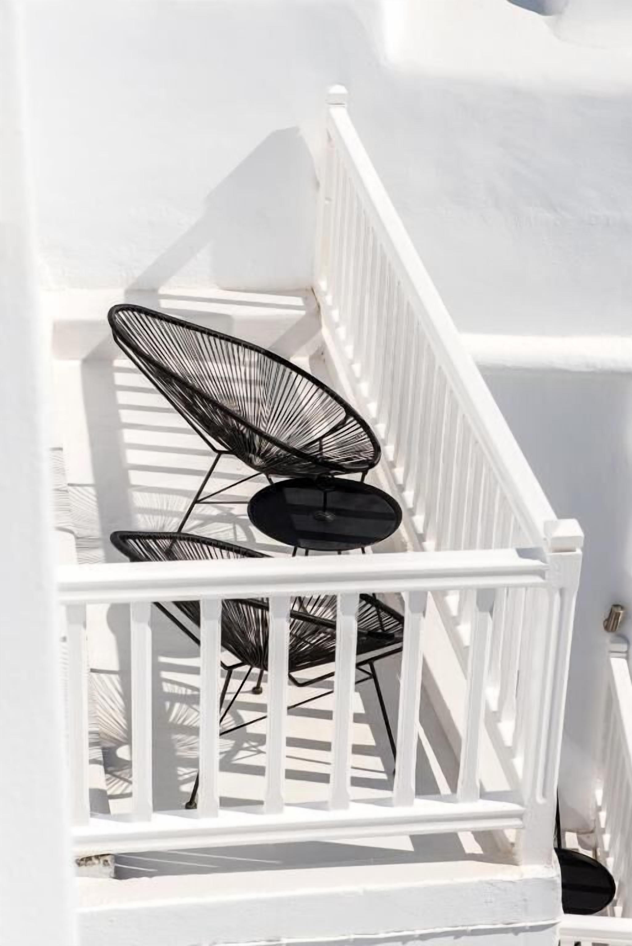 A white balcony with a white railing, two black wireframe chairs, and a small black table.
