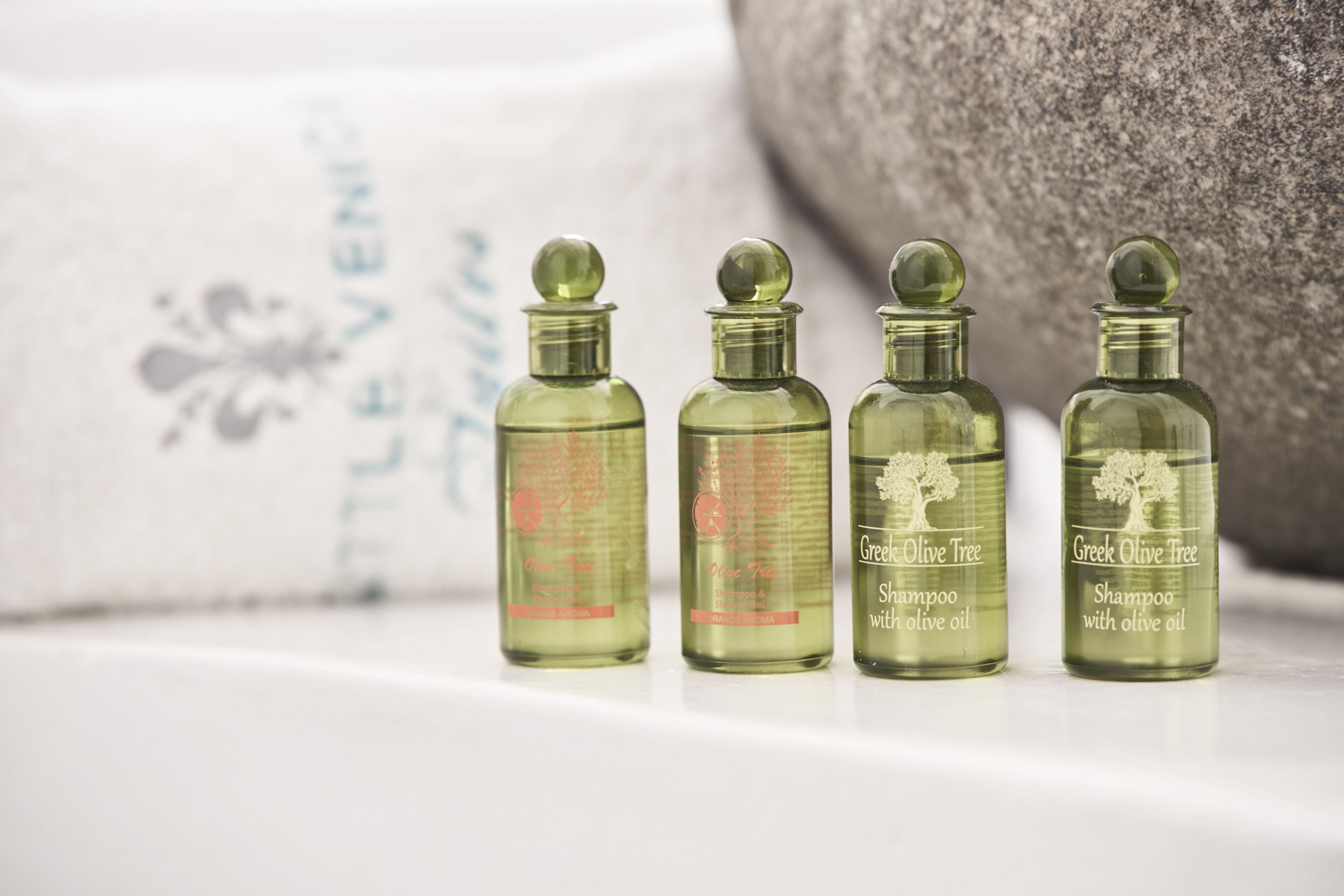 Four bottles of Greek Olive Tree shampoo with olive oil on a white surface.
