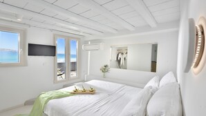 A modern bedroom with a large bed, a flat-screen TV, an air conditioning unit, and a view of the sea through a window.