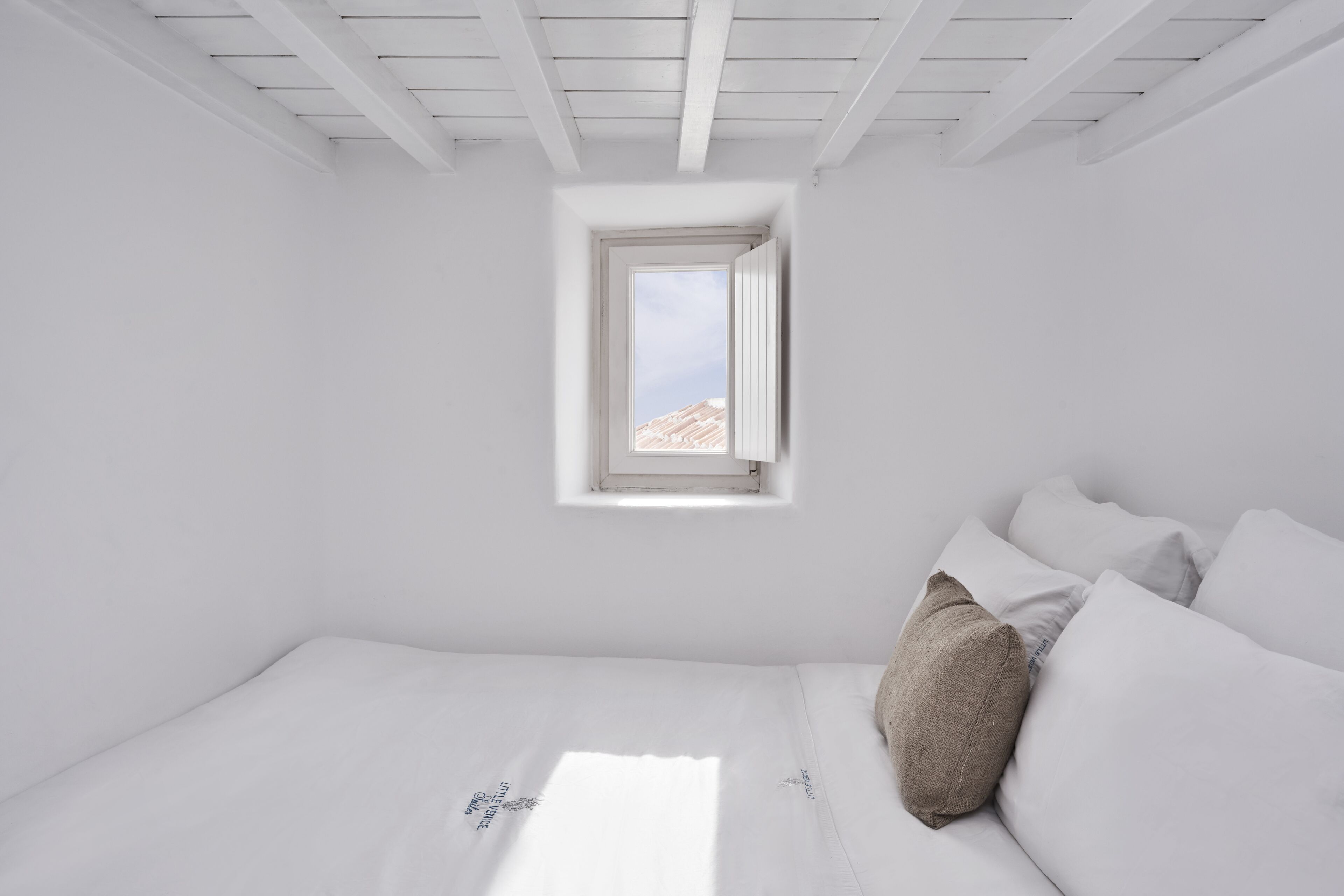 Ein schlicht eingerichteter Raum mit einem Bett, einem kleinen Fenster und Blick auf die Berge.