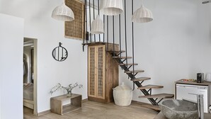 A modern kitchen with a wooden staircase, hanging pendant lights, and a small dining area with a coffee maker.
