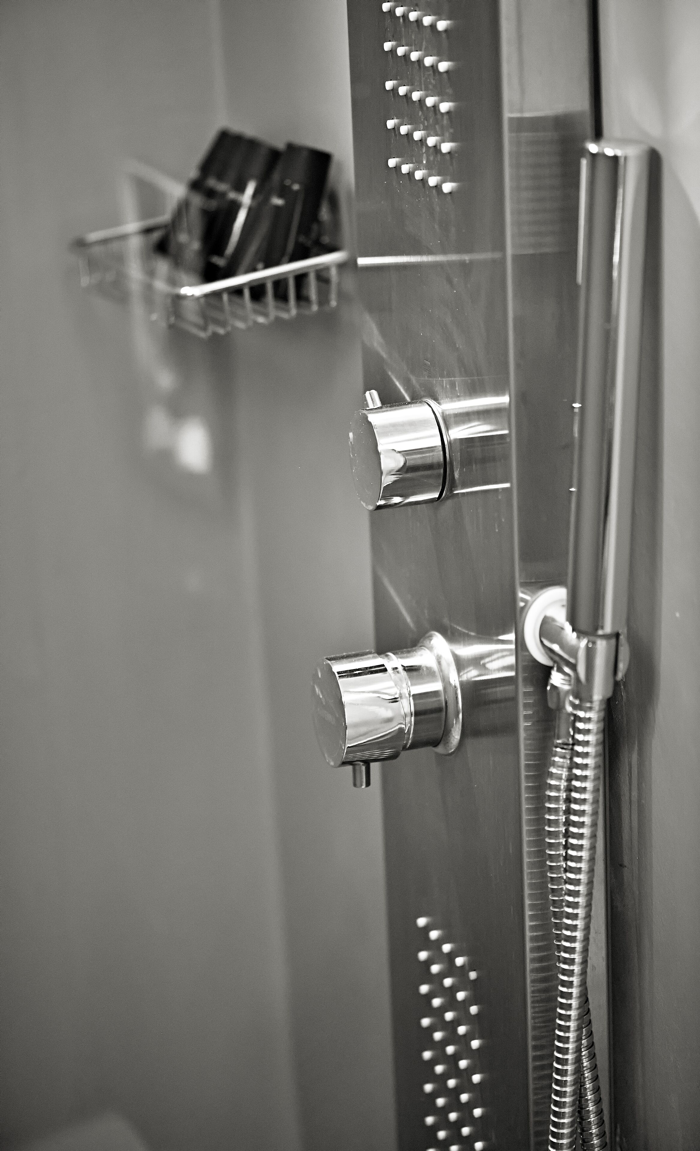 A metallic shower control panel with multiple handles and a flexible hose.