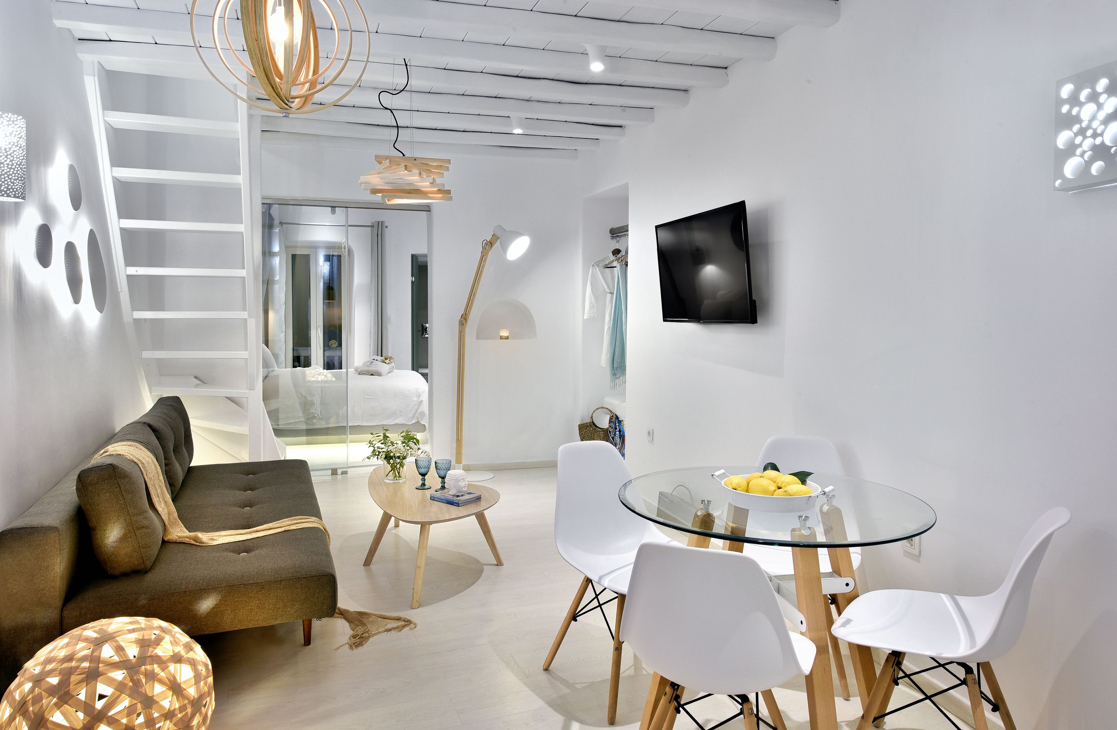 A modern living room with a sofa, a glass dining table, and a TV mounted on the wall.