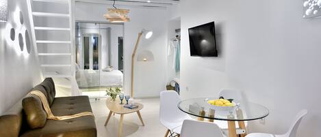 A modern living room with a sofa, a glass dining table, and a TV mounted on the wall.